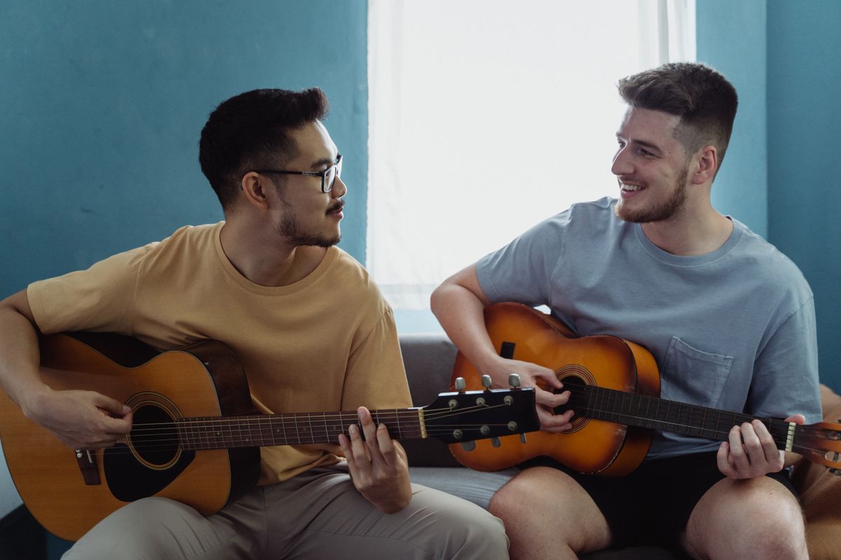 Birlikte keyifle akustik gitar çalan iki kişi